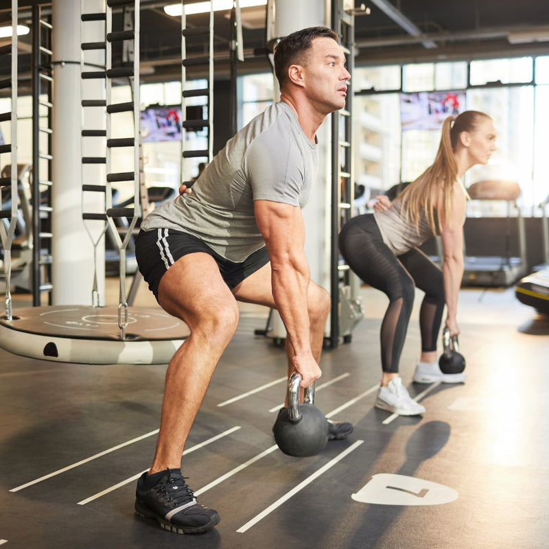 Two people exercising with kettlebells in a gym setting