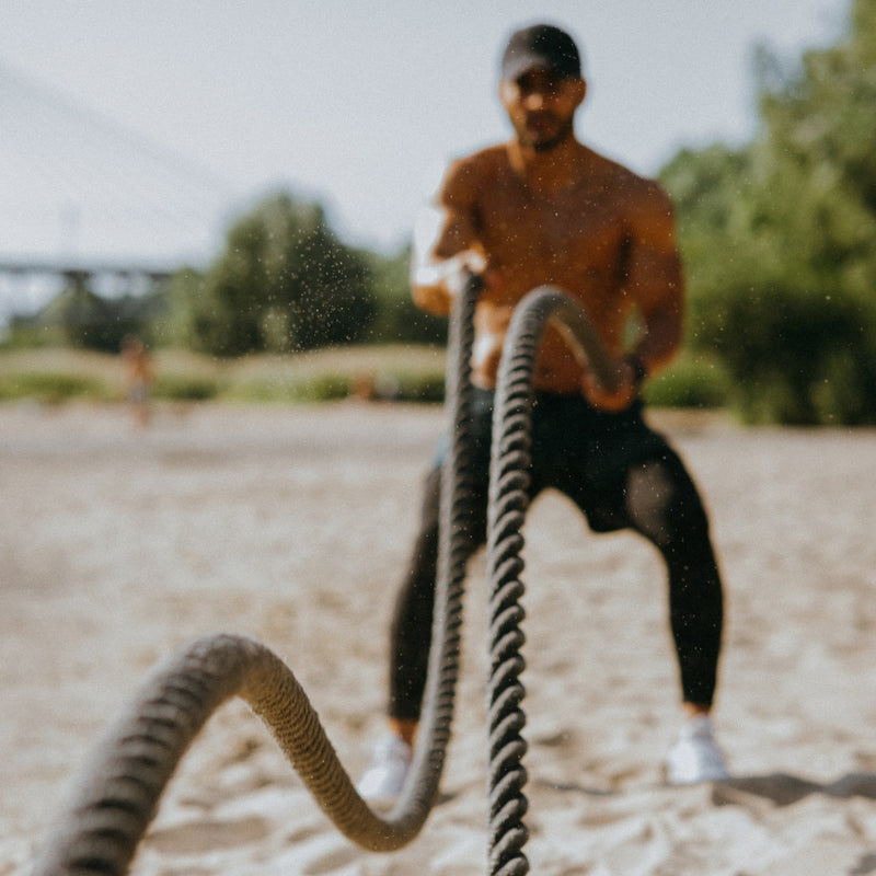 Person using battle ropes outdoors on a sandy surface with trees in the background