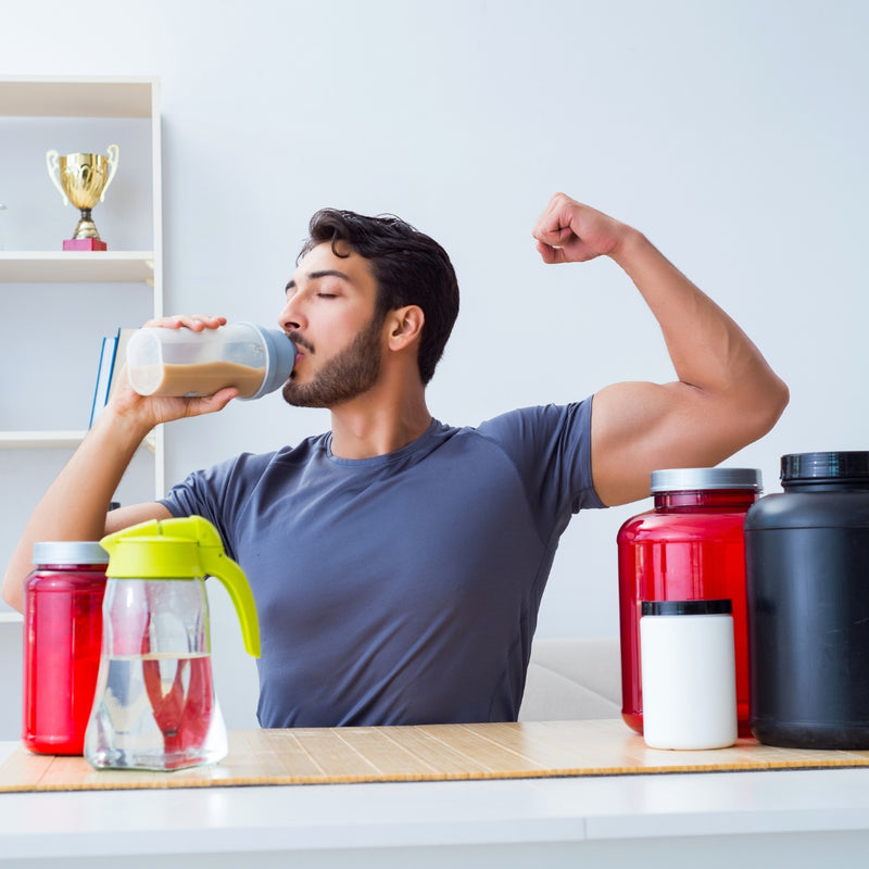 Man drinking a protein shake with supplement containers on a table