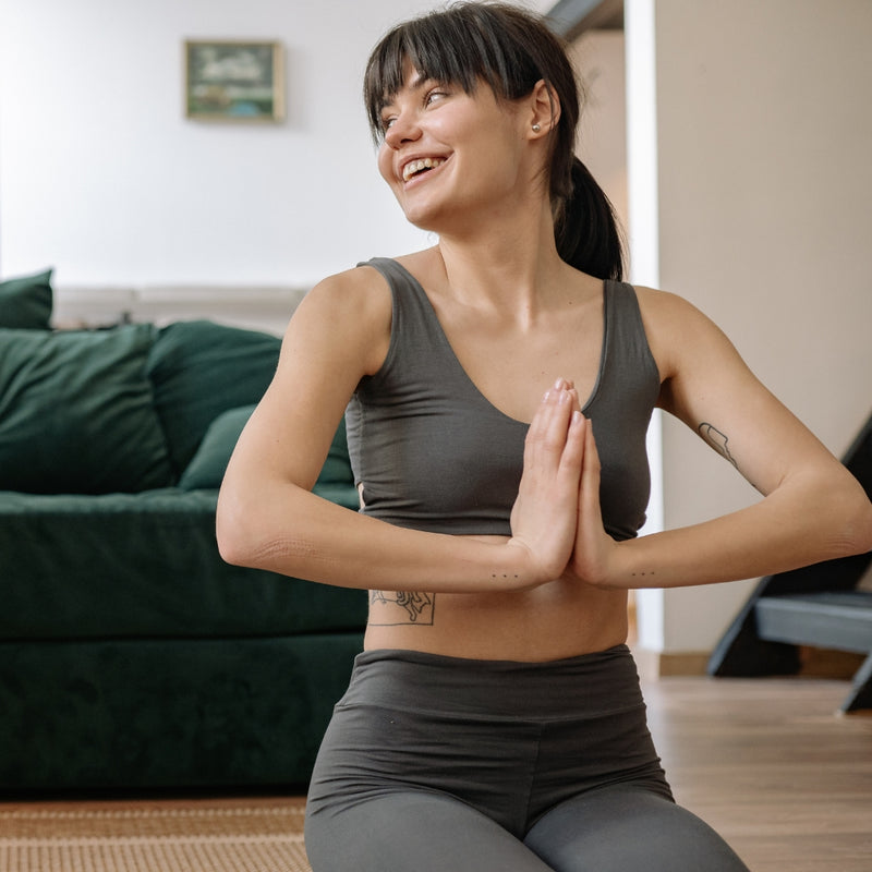 Woman in gray athletic wear sitting with hands together in a yoga pose in a living room.