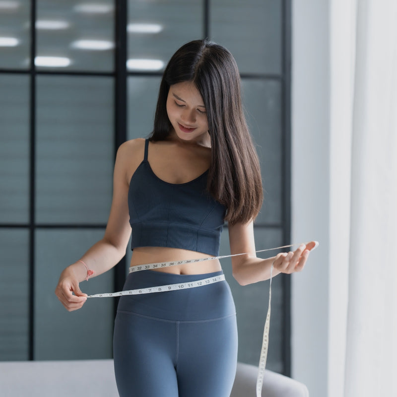 Woman measuring her waist with a tape measure in a modern indoor setting