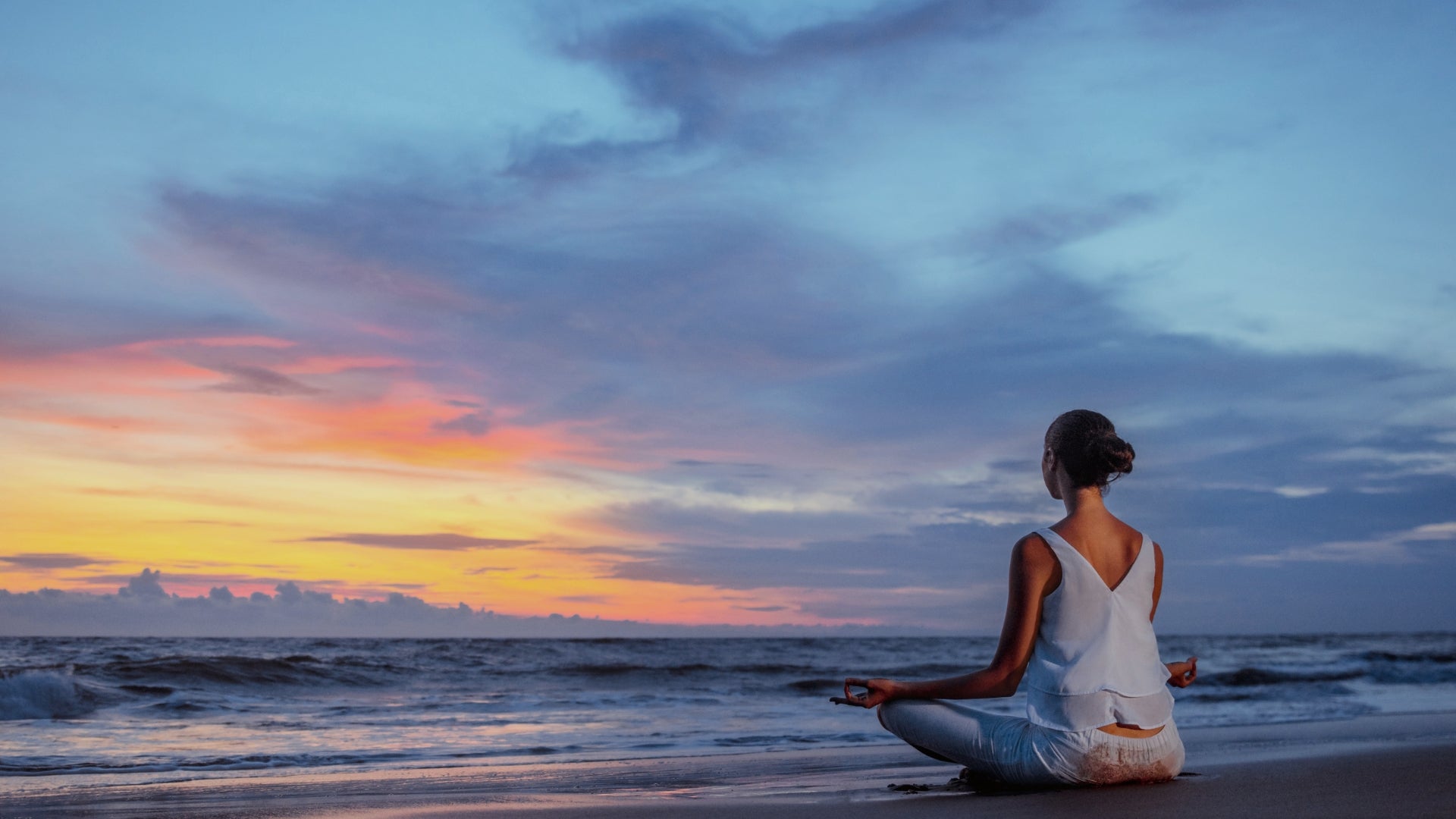 Woman sitting in lotus pose meditating on beach at sunset