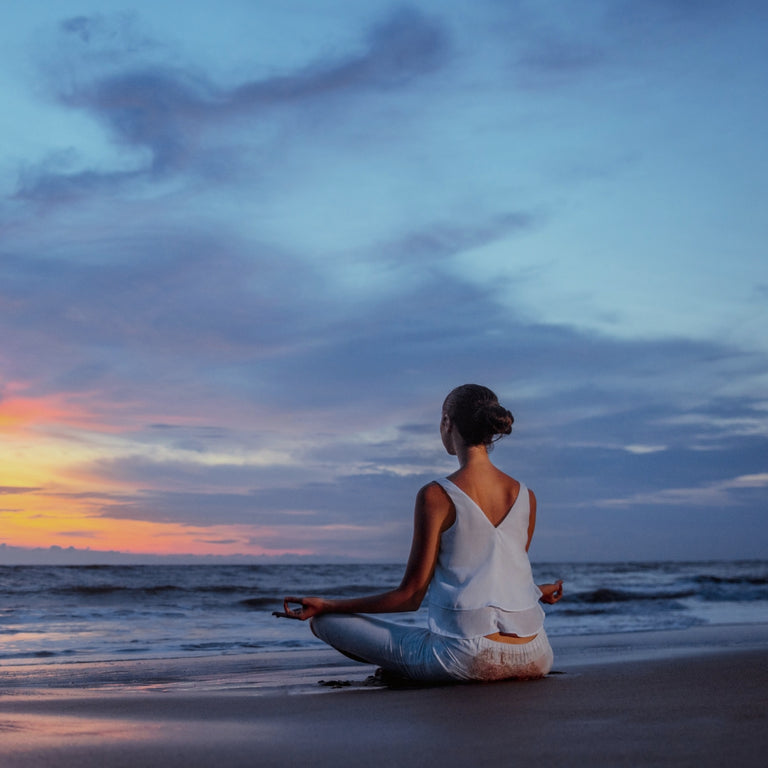 Woman sitting in lotus pose meditating on beach at sunset